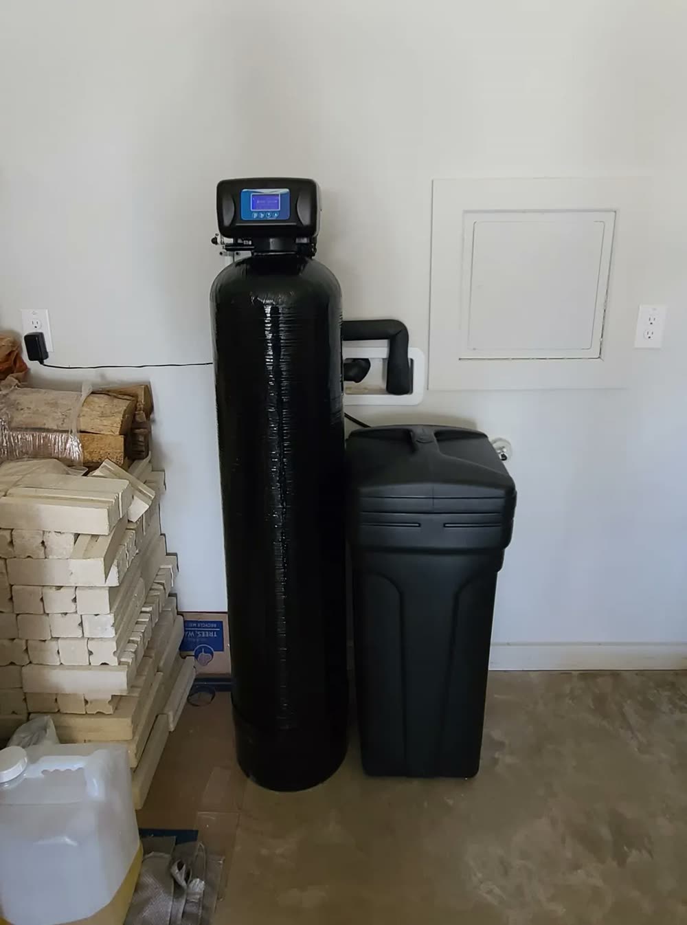 Whole-home water softener system installed against a garage wall